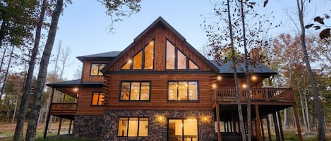 A two-story log cabin with a stone foundation, large windows, and a deck.