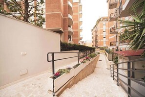 A narrow pathway flanked by residential buildings with balconies, stone flooring, and flower planters. - BuddyRent - Villa Pamphili - 6 ospiti (Roma)