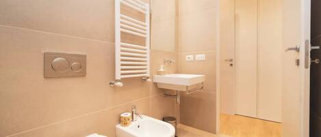 Un baño moderno con inodoro, bidé, lavamanos, toallero y una puerta.