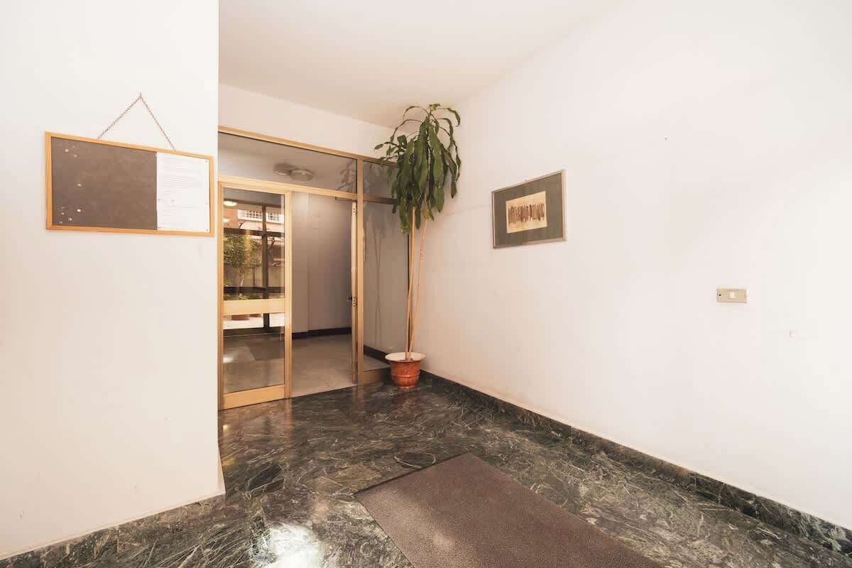 Un corridoio con pavimento in marmo, una pianta in vaso, un quadro appeso alla parete e una porta in vetro che dà su un'altra stanza.