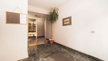 Ein Flur mit Marmorboden, einer Zimmerpflanze, einem gerahmten Bild an der Wand und einer Glastür zu einem weiteren Raum.