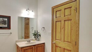 A bathroom with wooden cabinets, a sink, a mirror, a door, and a trash bin. - Black Pines Lodge (Swanton)