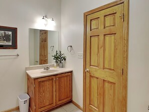 Un baño con armarios de madera, un lavamanos, un espejo, una puerta y un cubo de basura.