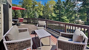Eine Terrasse im Freien mit Sitzgelegenheiten und einem Tisch, umgeben von Bäumen und blauem Himmel.