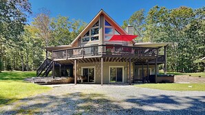 A two-story lodge with a balcony, a covered patio, and a gravel driveway. - Black Pines Lodge (Swanton)