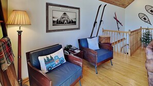 A cozy living room with a wooden ceiling, a framed picture, and skis leaning against the wall. - Black Pines Lodge (Swanton)