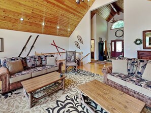 A spacious living room with wooden flooring, two sofas with patterned upholstery, a coffee table, and a staircase leading to another level. - Black Pines Lodge (Swanton)