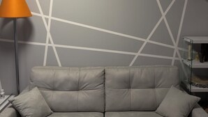 Una sala de estar moderna con un sofá gris, una lámpara de pie y un diseño geométrico en la pared.