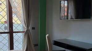 Habitación de hotel con cama, escritorio, silla, televisor y ventana con cortinas.