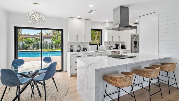 Una cocina moderna con una isla grande, armarios blancos y vistas a una piscina.