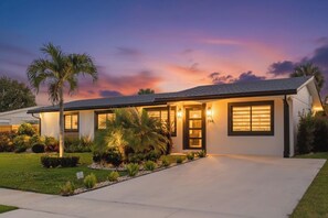 Une maison moderne de plain-pied, dotée d’une pelouse bien entretenue, d’un palmier et d’une allée menant à l’entrée.