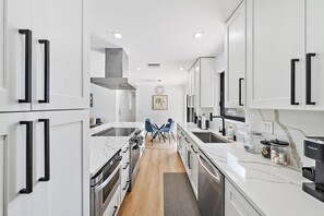 Une cuisine moderne avec des meubles blancs, des appareils en acier inoxydable et un plan de travail en marbre.