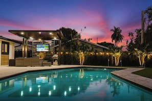 Une piscine avec un espace bar, des palmiers et un ciel au coucher du soleil.
