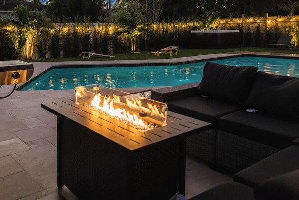 A poolside area with a fire feature, outdoor seating, and a view of the pool.