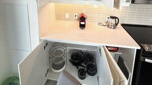 Een kleine keuken met witte kastjes, een magnetron en een koffiezetapparaat op het aanrecht.