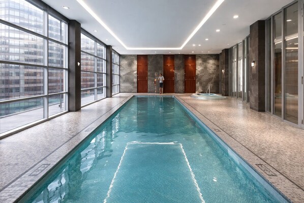 Una piscina interior larga con agua cristalina, rodeada de amplios ventanales y paredes de piedra.