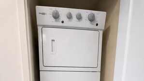 Een kleine, witte wasruimte met een voorlader wasmachine en droger, inclusief bedieningsknoppen en een klein kastje voor opslag.