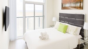 Een hotelkamer met een groot bed, een flatscreen-tv aan de muur, een schilderij boven het bed en een balkon met uitzicht.