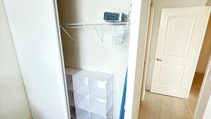Een inloopkast met een schuifdeur, een wit opbergmeubel en een blauwe bezem die tegen de muur staat.