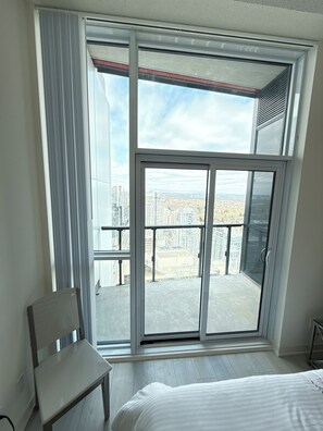 Una habitación de hotel con un gran ventanal corredero que da a un balcón con vistas a la ciudad.