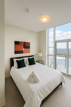 Habitación de hotel moderna con una cama grande, vista al mar y una lámpara de techo.