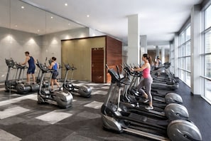 Une salle de sport dotée de nombreux tapis de course disposés en rangées, de grandes fenêtres et d’un aménagement intérieur moderne.