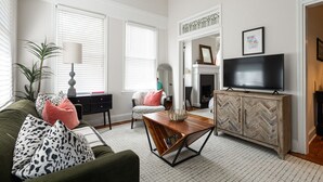 Ein Wohnzimmer mit einer Couch, einem Couchtisch, einem Fernseher, einem Kamin und einem Schrank mit Fischgrätenmuster.