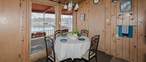 Una habitación con paneles de madera, una mesa redonda para cuatro personas, un reloj en la pared y vistas a un cuerpo de agua a través de una ventana.