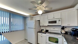Una cucina con mobili bianchi, un frigorifero, un forno a microonde, un forno e una ventola a soffitto.