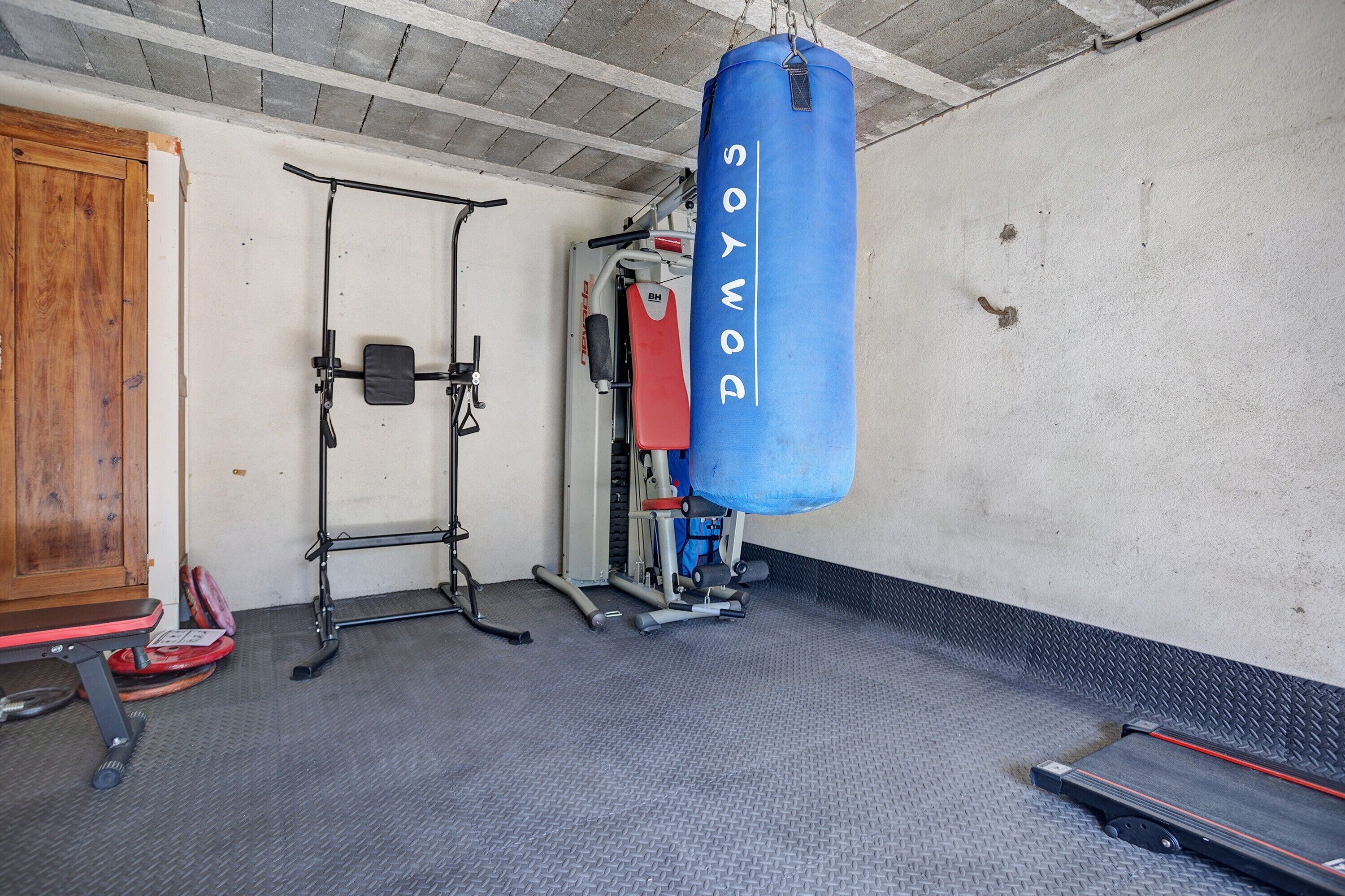 Ein Fitnessstudio mit einem blauen Sandsack, einer Gewichthecke und einem Laufband.