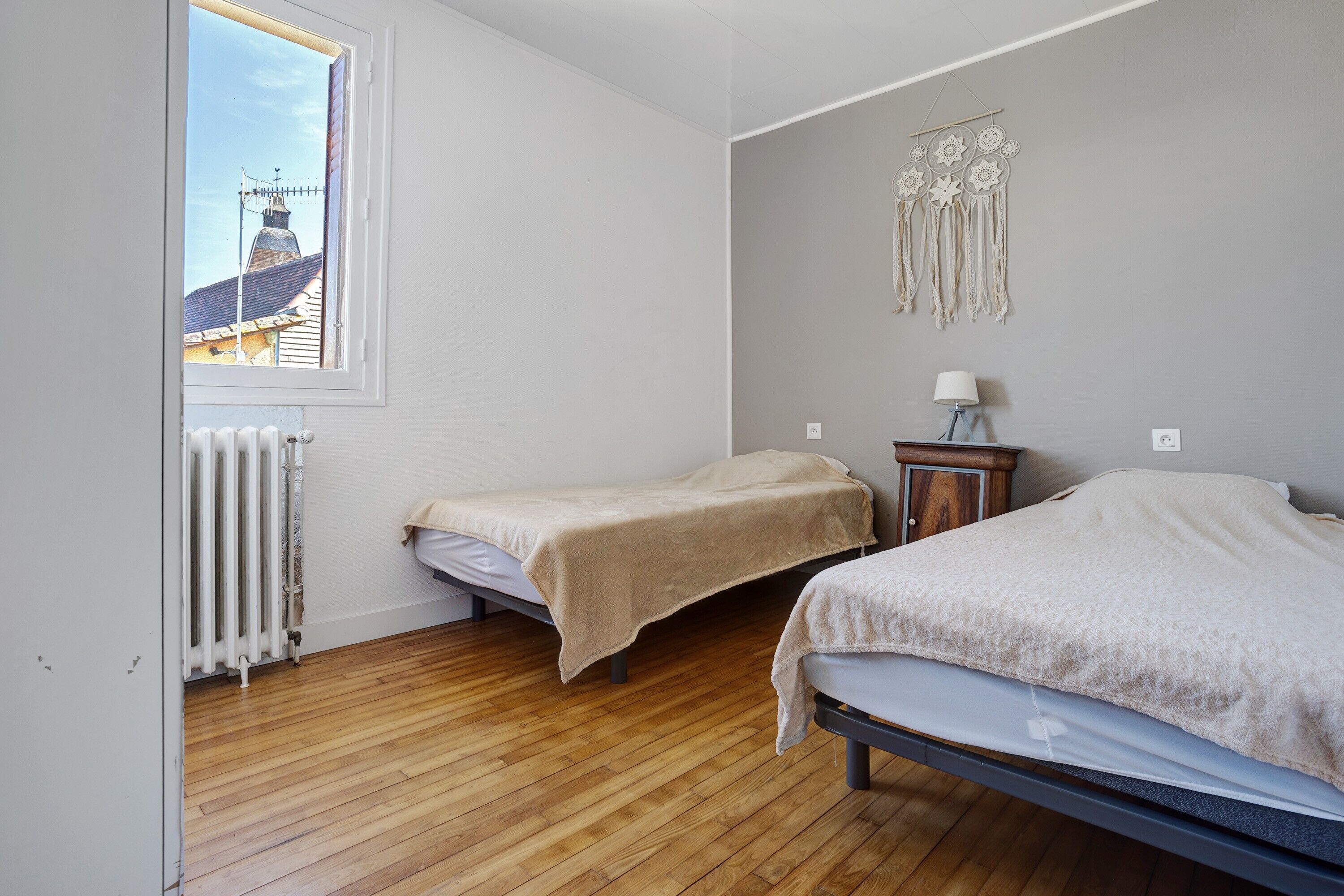 Une chambre avec deux lits, un radiateur, une fenêtre et un élément décoratif mural.