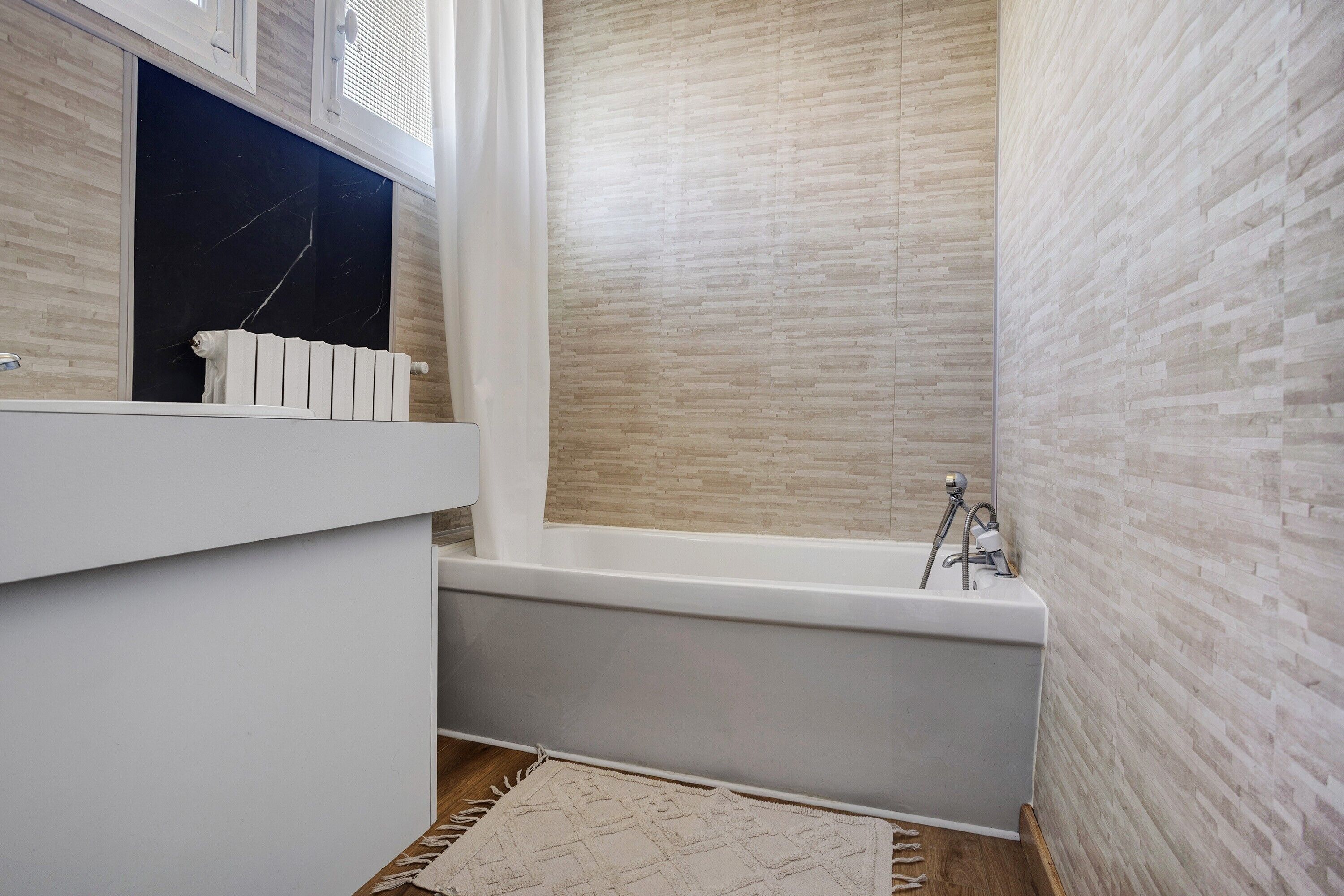 Un baño con bañera, lavamanos blanco y encimera de mármol.
