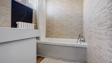 Un baño con bañera, lavamanos blanco y encimera de mármol.