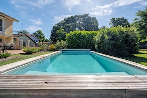 Une piscine rectangulaire avec une terrasse en bois, située dans un quartier résidentiel.