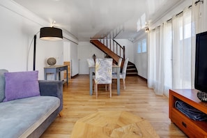 Ein Wohnzimmer mit Sofa, Couchtisch, TV-Schrank, einer Treppe und einem Essbereich mit Stühlen und Tisch.