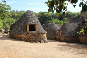 Ein traditionelles Gebäude mit steinbedecktem Dach und einer zentralen Tür, umgeben von ähnlichen Bauten in ländlicher Umgebung.