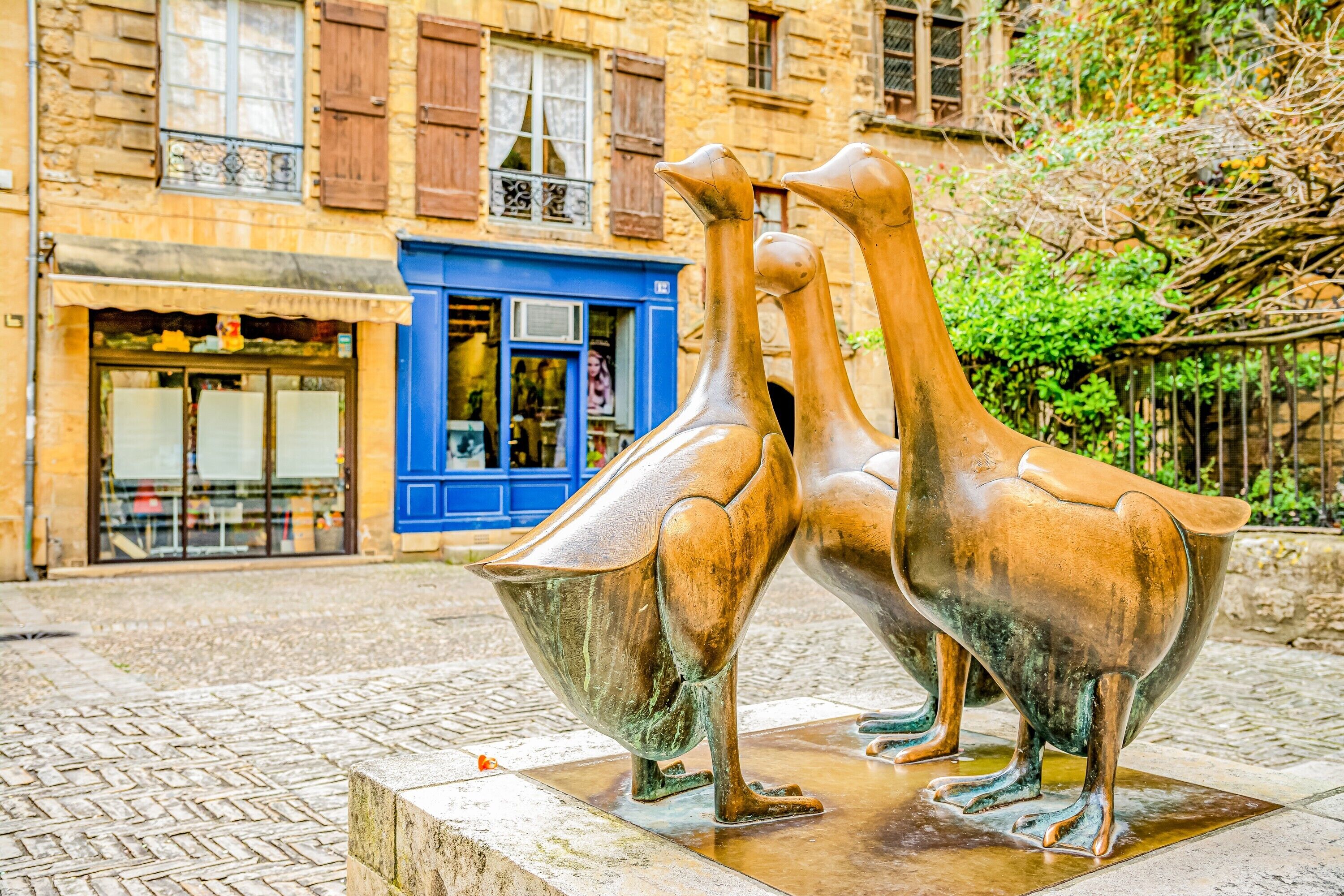 A bronze sculpture of two birds in a public square with a building in the background.