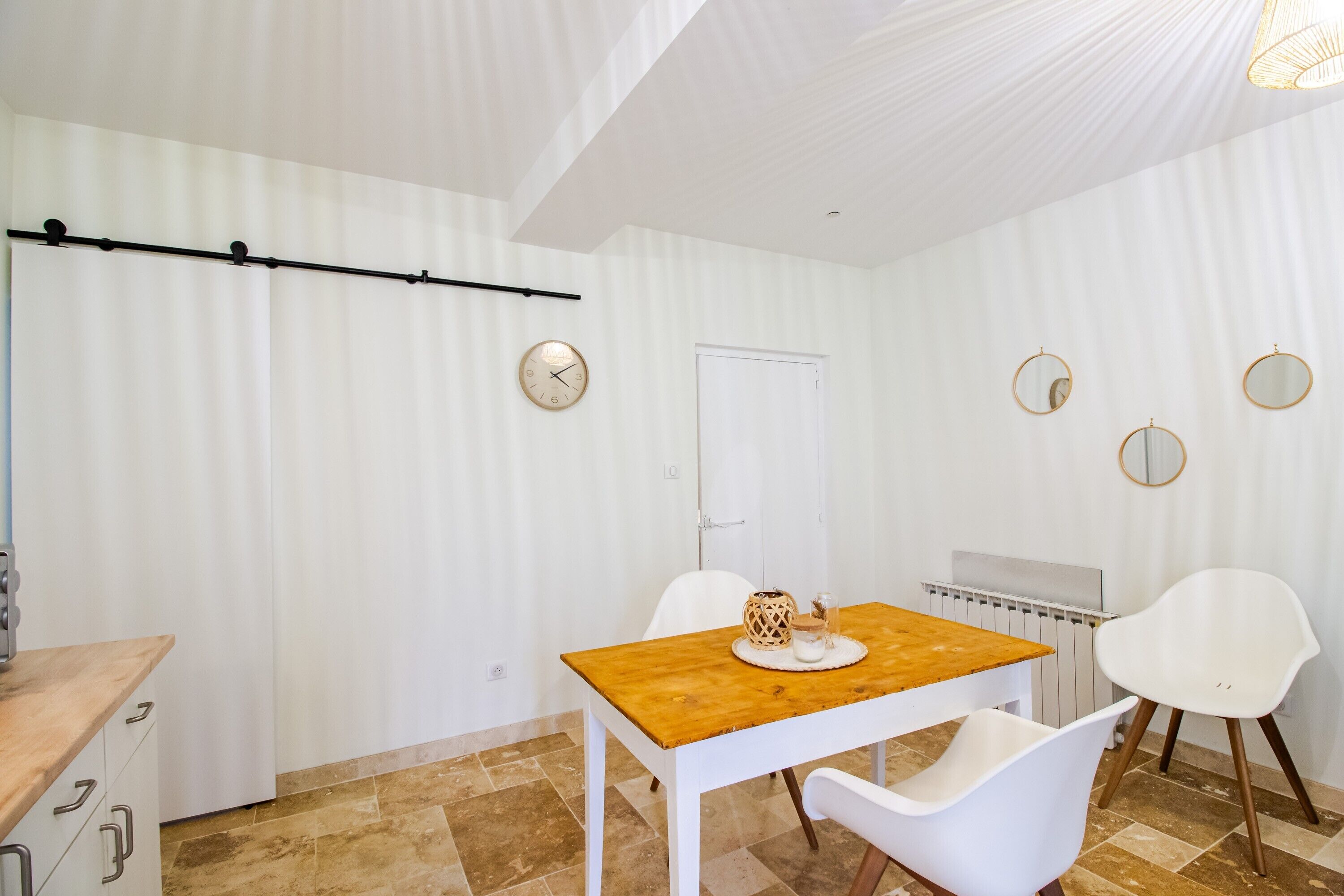Zona de menjador amb taula de fusta, cadires blanques, un radiador i una porta blanca.