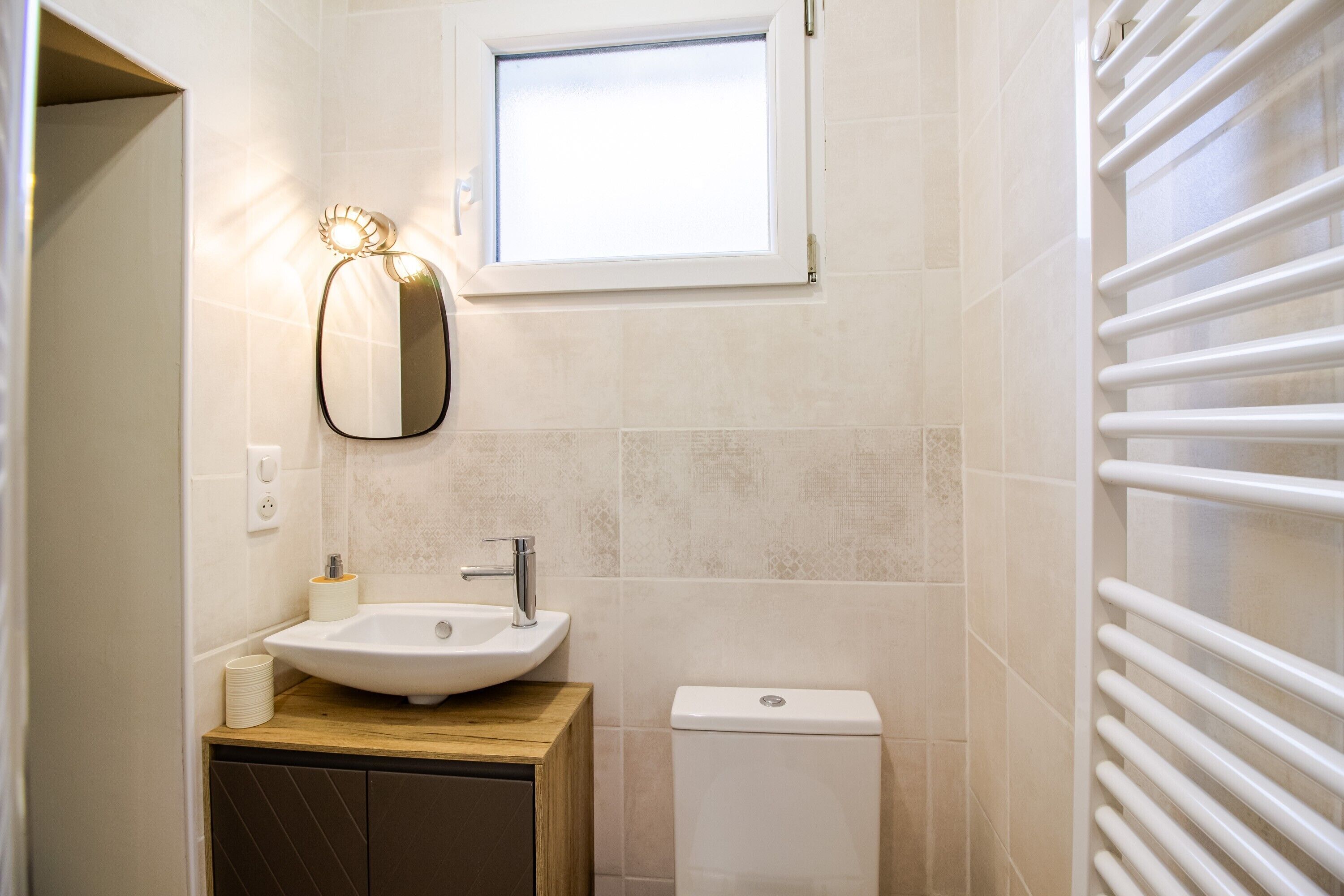 A bathroom with a sink, mirror, toilet, and a window.
