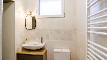 A bathroom with a sink, mirror, toilet, and a window.