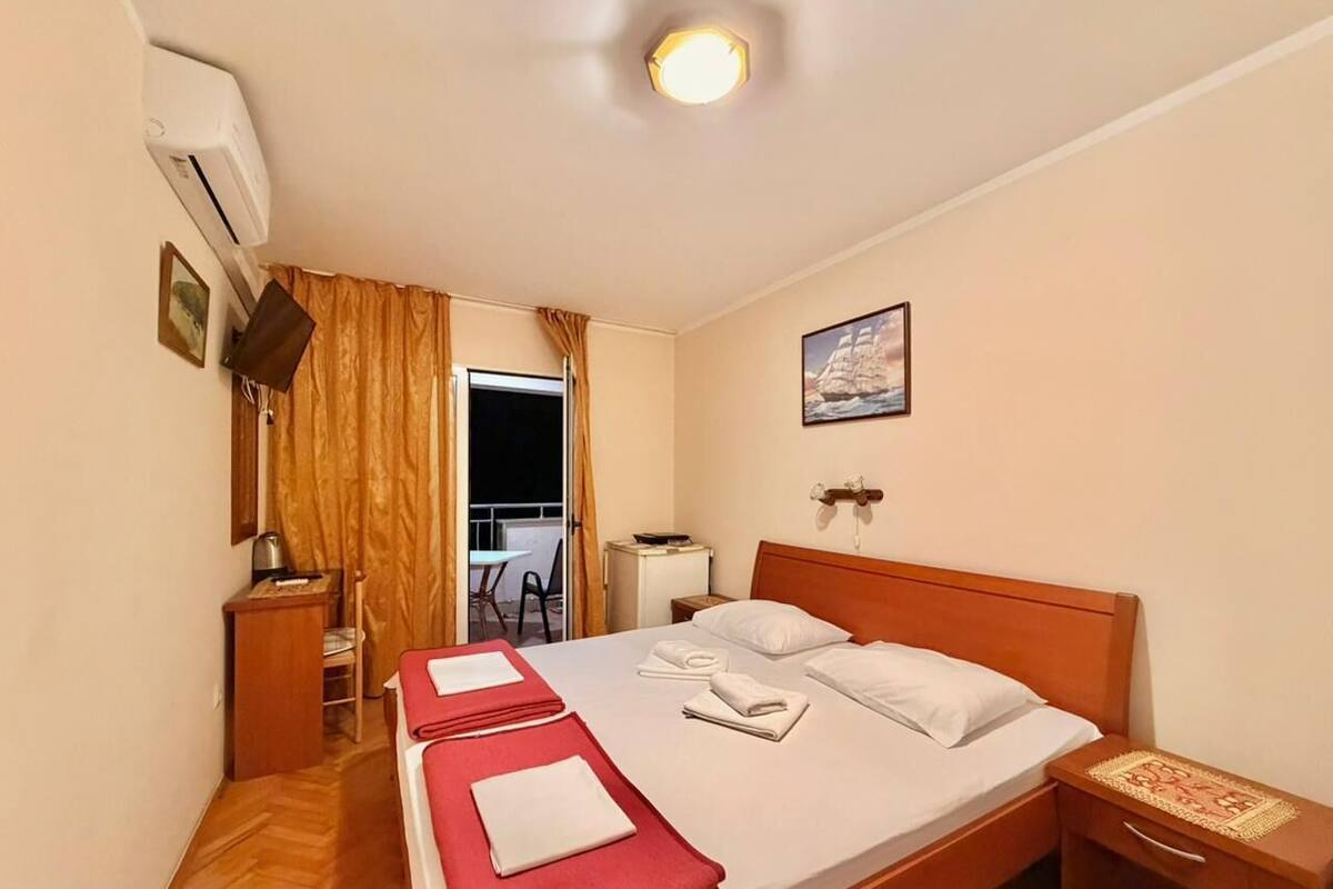 A hotel room with a bed, a bedside table, a lamp, a chair, a small table, and a window with curtains.
