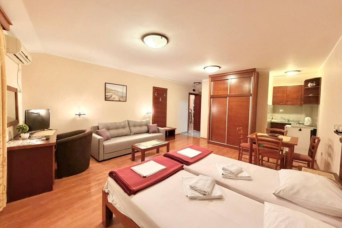 A hotel room with two beds, a sofa, a desk, a TV, and a kitchenette.