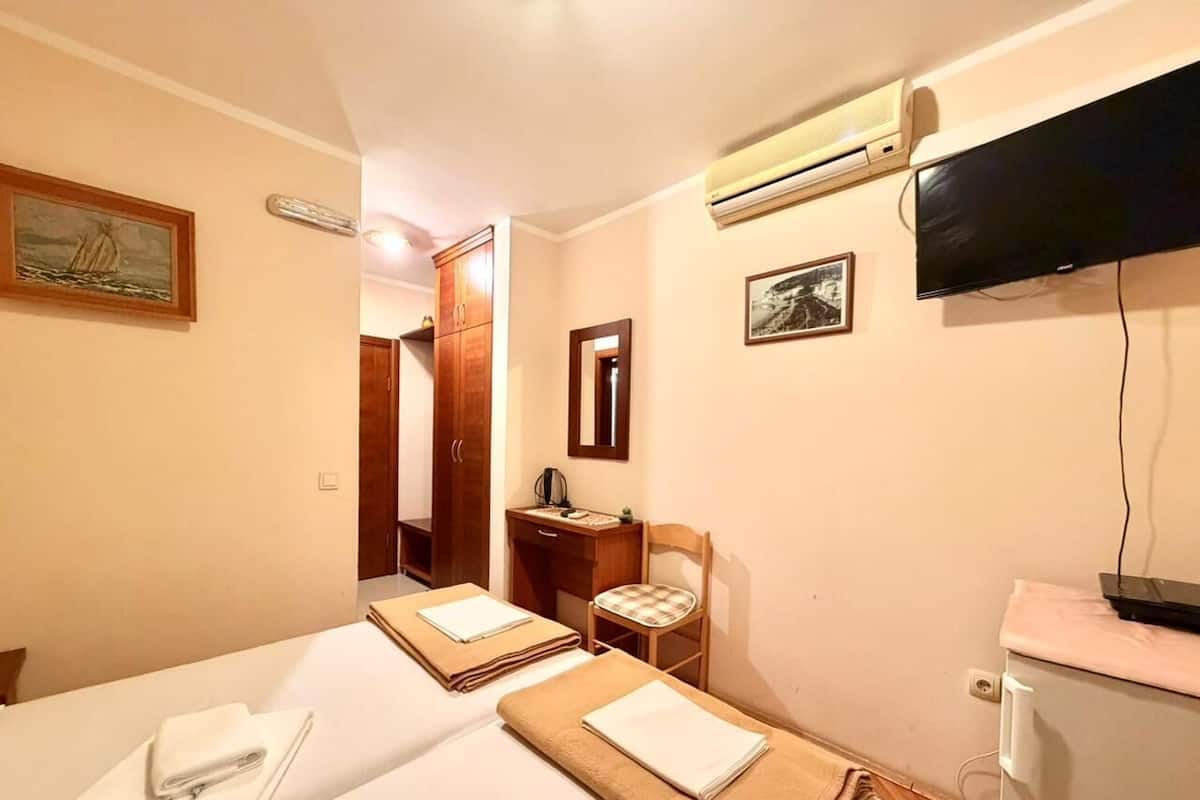 A hotel room with two beds, a desk, a chair, a TV, and an air conditioning unit.