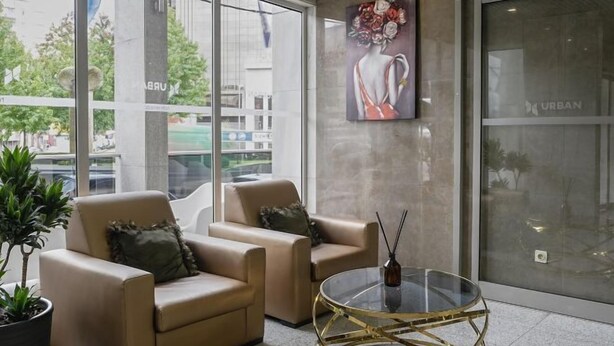 Un moderno vestíbulo con dos sillones color beige, una mesa de centro de vidrio y un ventanal con vista a la calle.