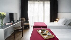 Habitación de hotel con cama, escritorio con silla, televisor y bandeja de desayuno sobre la cama.