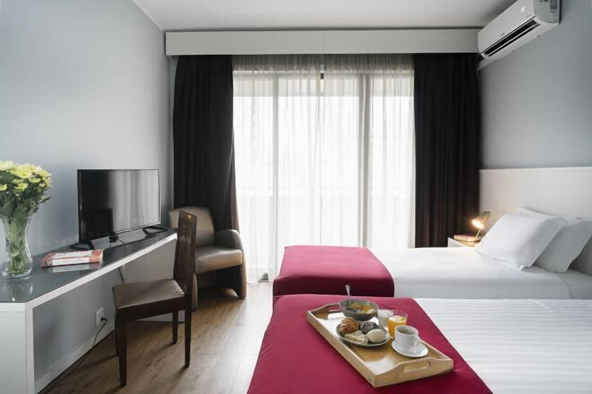 A hotel room with a bed, a desk with a chair, a TV, and a breakfast tray on the bed.