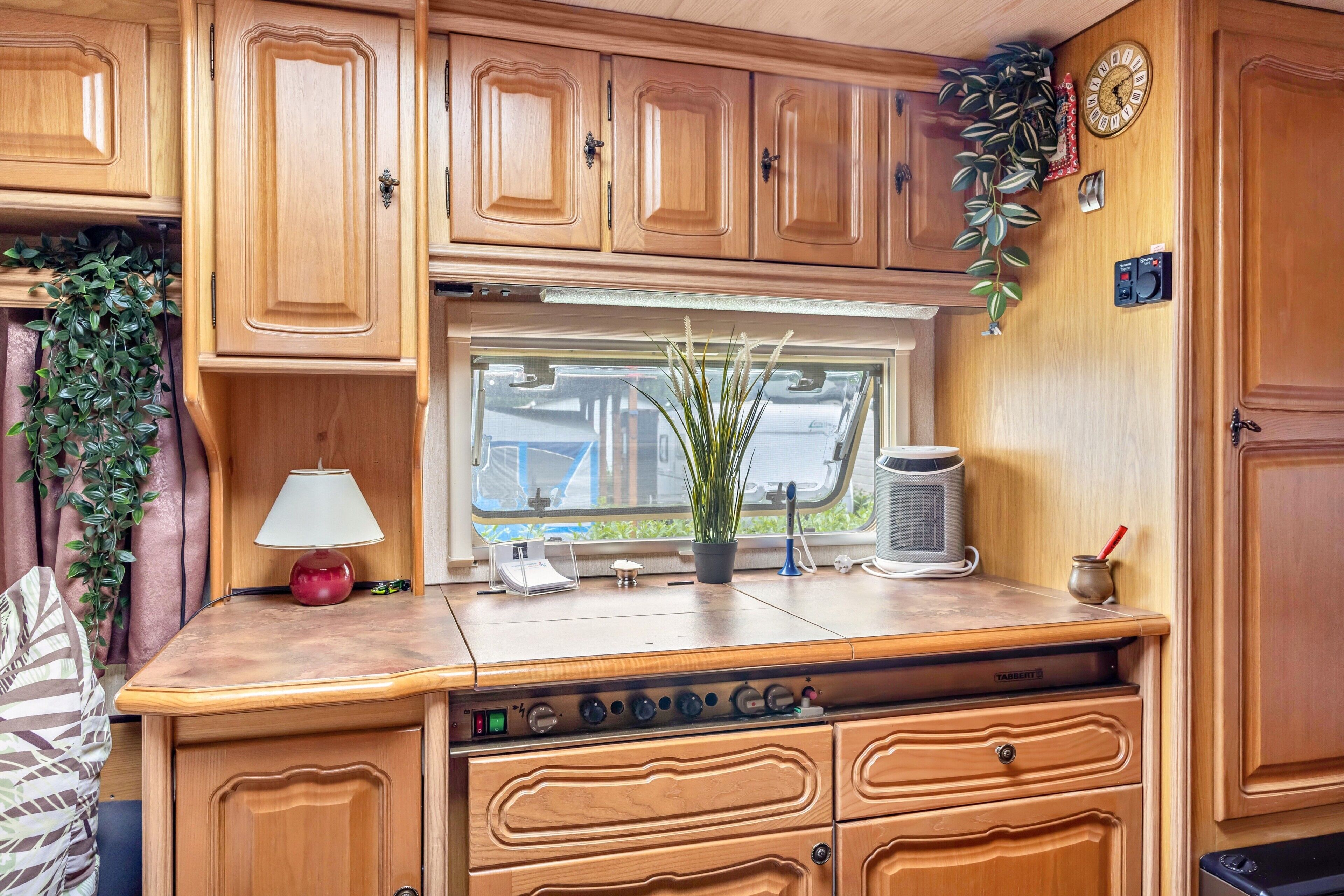 A compact kitchen with wooden cabinets, a window, a coffee maker, and a plant.