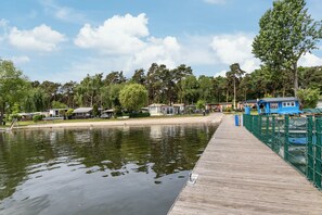 Un muelle de madera que se adentra en un cuerpo de agua tranquilo, rodeado de árboles y pequeños edificios.