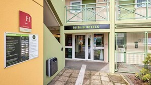 Entrada de un hotel B&B con fachada verde, un letrero 'H' rojo y una puerta de acceso visible.