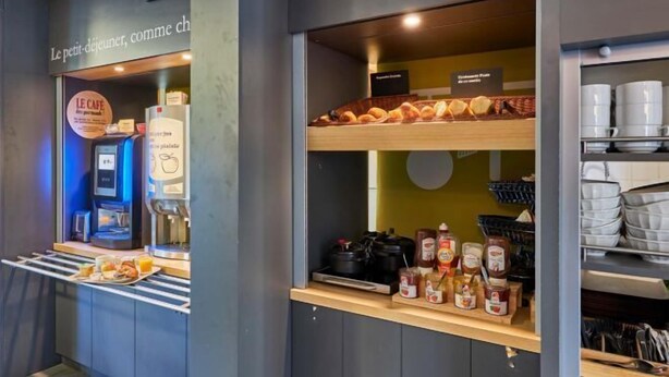 Una barra de desayuno con una máquina de café, un cartel que dice 'Le Petit Déjeuner' y diversas salsas y pasteles.